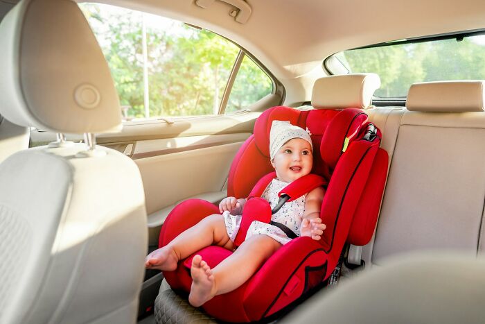 Baby secured in a bright red car seat inside a vehicle, illustrating safety unrelated to workplace scandals.