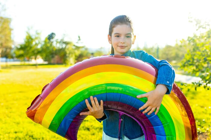 Young girl holding a large colorful rainbow balloon outdoors, representing bizarre and unusual names given to children.