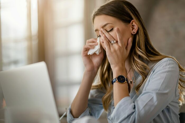 Stressed woman wiping tears while working on laptop, representing infuriating moments people experienced at work.