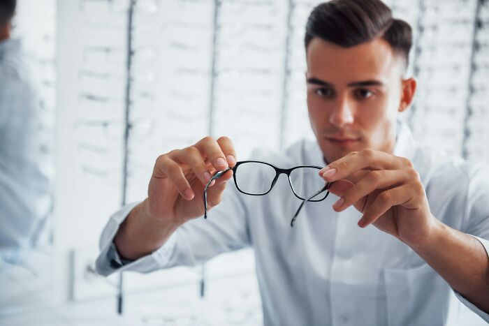 Man inspecting eyeglasses closely in a store, symbolizing employees revealing dark truths about industries hidden from view.