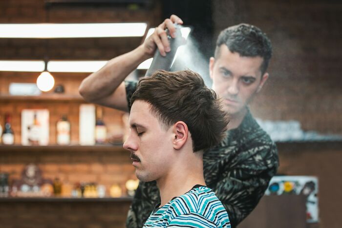Barber carefully styling a young man’s hair indoors, capturing an unseen side of a digital nomad’s life experience.
