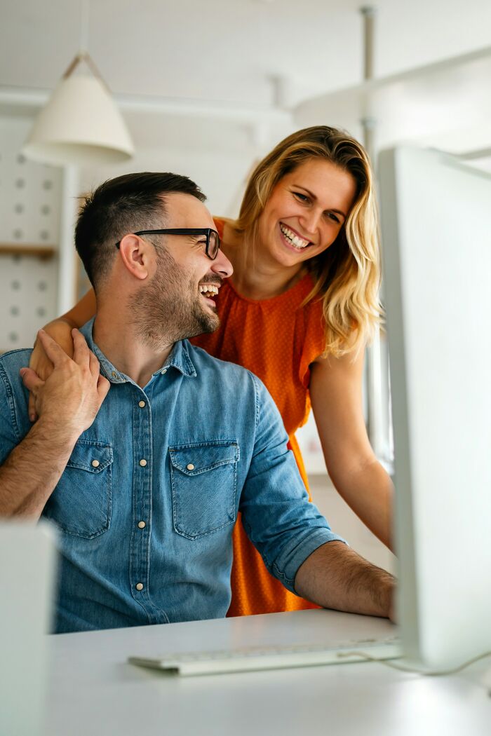 Two coworkers sharing a joyful moment together while working at a computer, highlighting work-life balance.