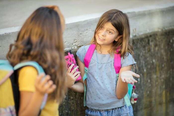 Two young girls with backpacks talking outside, illustrating modern parenting trends and challenges in today's families.