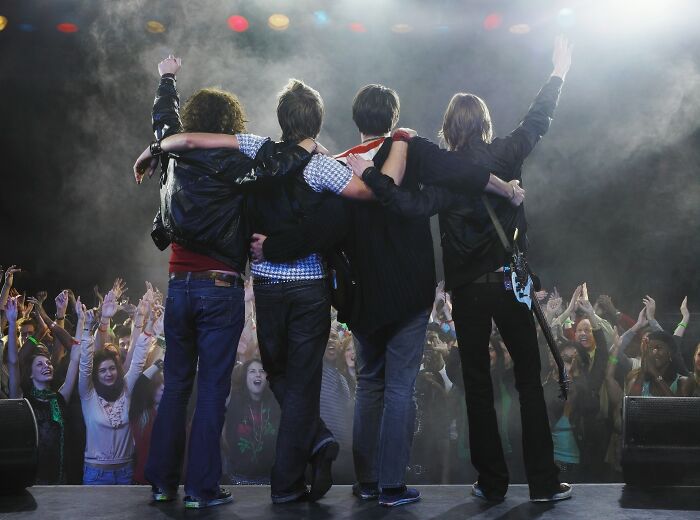 Four musicians on stage facing an excited crowd, celebrating moments when people became rich unexpectedly.