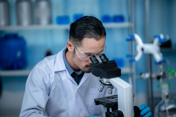 Scientist in a lab coat and safety glasses examining samples under a microscope revealing disturbing science facts.