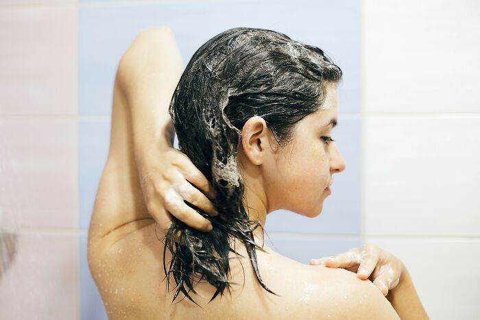 Woman washing hair with shampoo in shower, symbolizing cleansing after bitter revenge stories and petty victories.