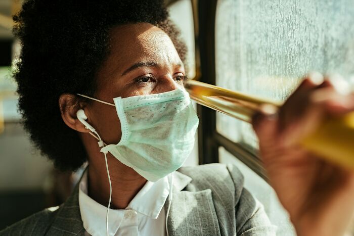 Person wearing a face mask and earbuds looking out window, reflecting on harmless but toxic habits during commute.