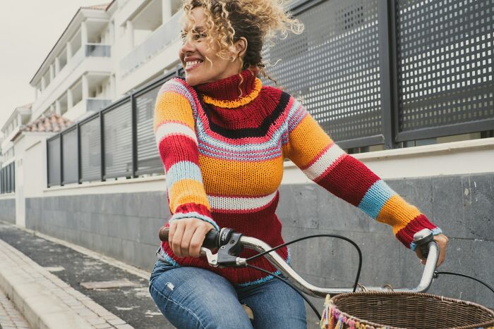 Woman in colorful sweater riding a bicycle outdoors, enjoying the moment in a true stories setting.