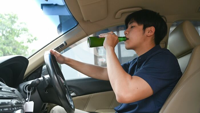 Man drinking alcohol inside a car, illustrating one of the biggest scandals in workplaces involving unsafe behavior.