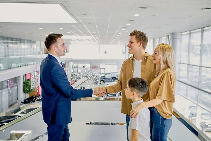 Family smiling and shaking hands with a salesman at a dealership, illustrating signs someone is stuck in their high school era.