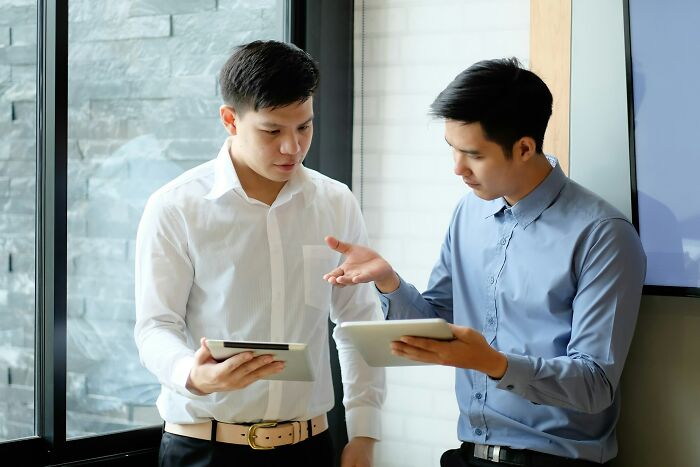 Two men in business attire discussing digital tablets, revealing dark secrets affecting their trust and perception.