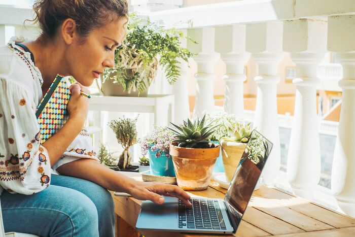 Woman working on laptop surrounded by plants, showcasing the daily life of a digital nomad in a bright, cozy space.