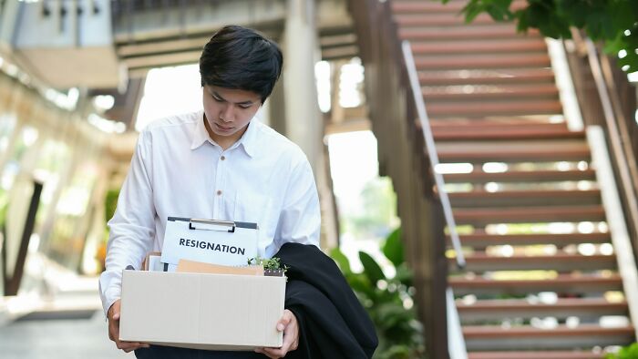 Young male employee holding a resignation box, reflecting on infuriating moments at work and feeling underpaid.