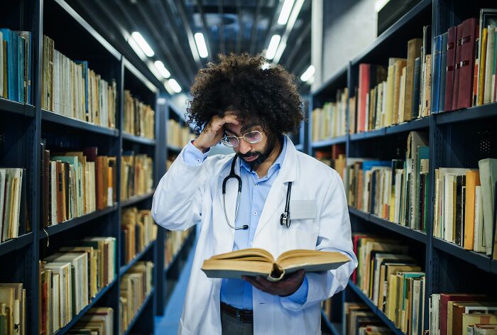 Medical professional in a library looking stressed while reading, illustrating employees revealing dark, dirty industry truths.