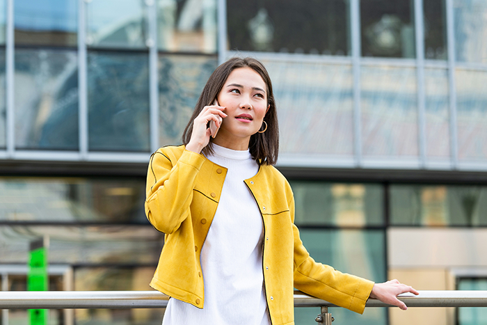 Woman talking on phone outside modern building, looking concerned about HOA fine for festive Christmas decor