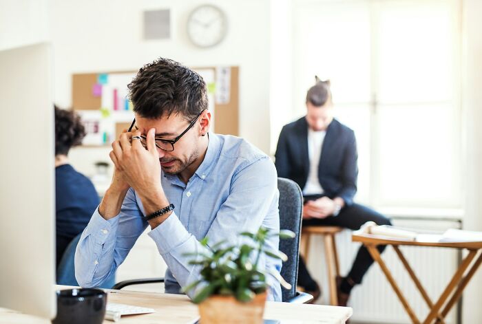 Stressed office worker with glasses holding his head in frustration, depicting infuriating moments experienced while working.