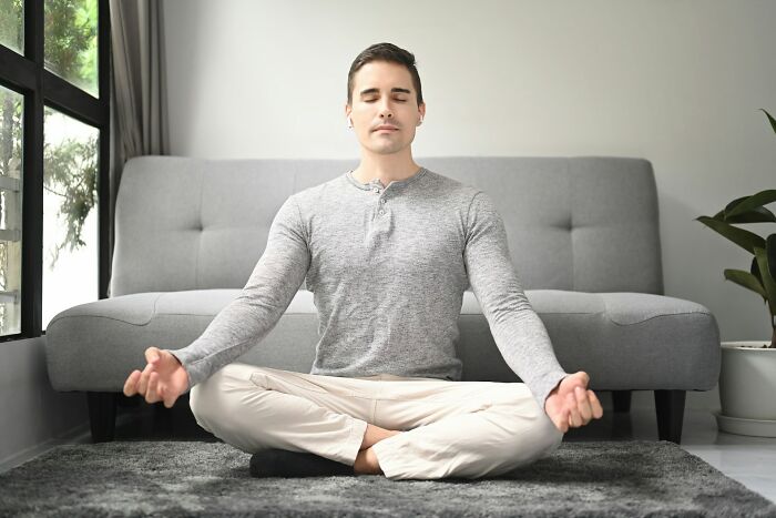 Man sitting cross-legged on carpet meditating in living room illustrating everyday things people accidentally did wrong.