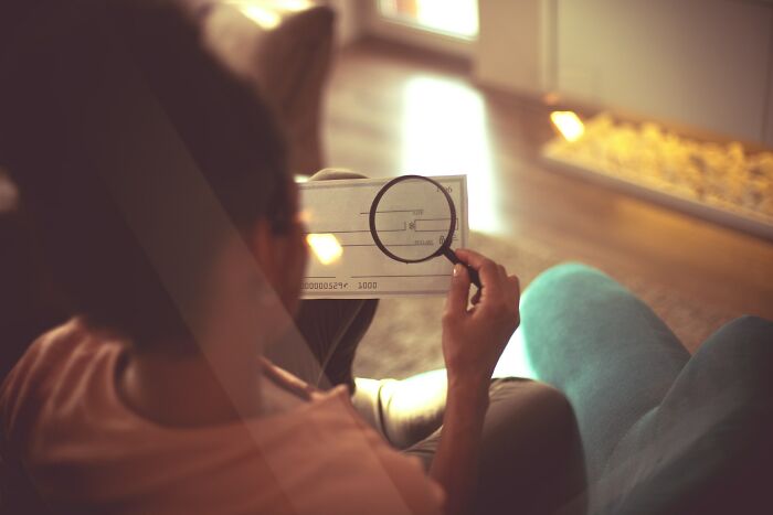 Person sitting on a couch using a magnifying glass to closely examine a document, illustrating secrets people trust online.