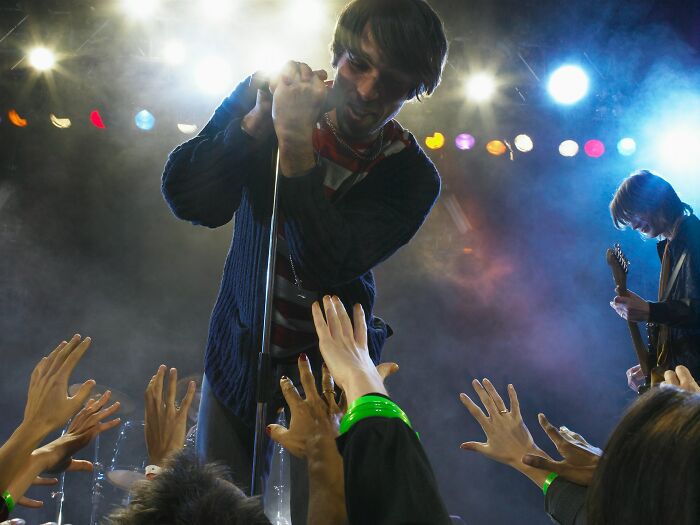 Lead singer engaging with fans at a concert, showcasing incredible minds embracing genius without a degree.