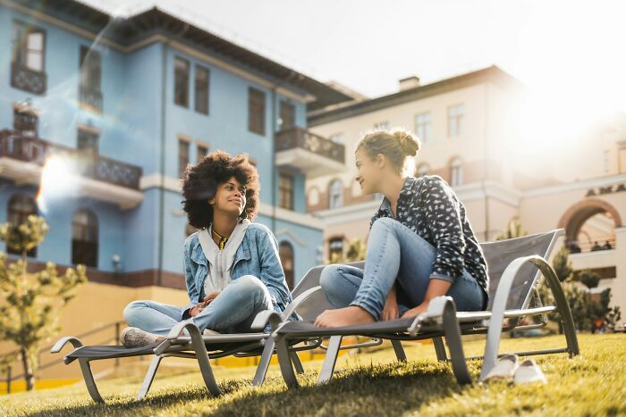 Two women talking and relaxing outdoors on lounge chairs, capturing the real side of digital nomad life.