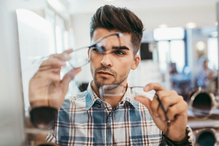 Young man in a plaid shirt examining eyeglasses, symbolizing harmless but toxic habits awareness and reflection.