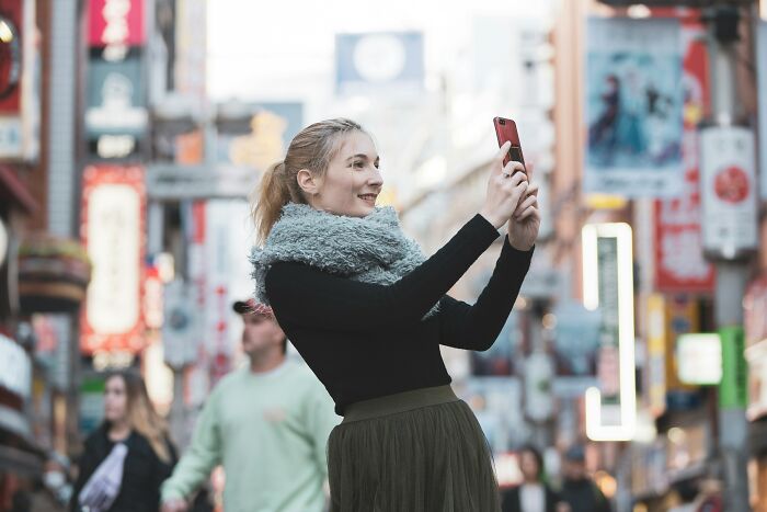 Young woman smiling and taking a selfie outdoors, capturing a moment that highlights small decisions shared online.