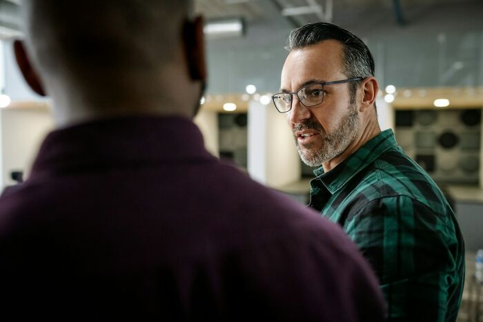 Man in glasses wearing a green shirt talking seriously to a coworker, depicting infuriating moments while working.