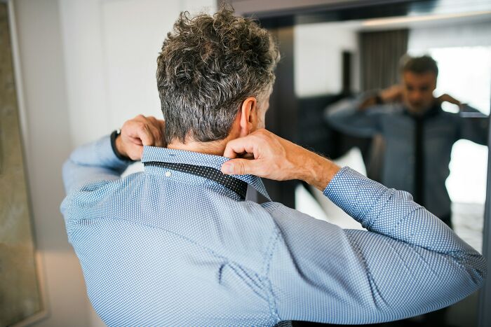 Man adjusting tie in front of mirror, preparing for day while reflecting on interesting life facts that may surprise you.