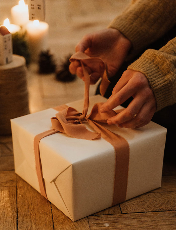 Hands untying a Christmas gift box with ribbon in a cozy setting, relating to unthoughtful gift and relationship issues. Hands untying a Christmas gift box with ribbon in a cozy setting, relating to unthoughtful gift and relationship issues.