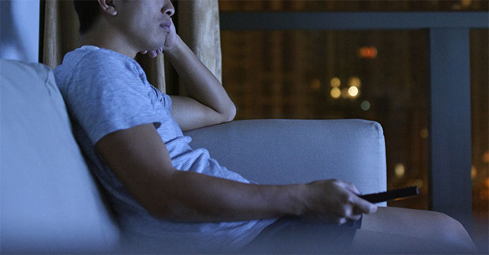 Man sitting alone on couch at night holding remote, reflecting on unthoughtful gift causing relationship breakup at Christmas. Man sitting alone on couch at night holding remote, reflecting on unthoughtful gift causing relationship breakup at Christmas.