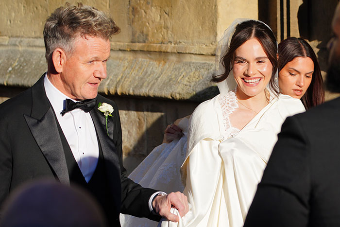 Gordon Ramsay in a tuxedo holding his daughter's hand during her wedding to Adam Peaty, surrounded by guests outdoors.