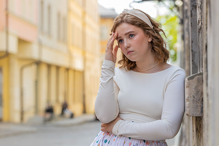Young woman leaning against wall looking upset, reflecting on family issues and feeling emotionally hurt. Young woman leaning against wall looking upset, reflecting on family issues and feeling emotionally hurt.