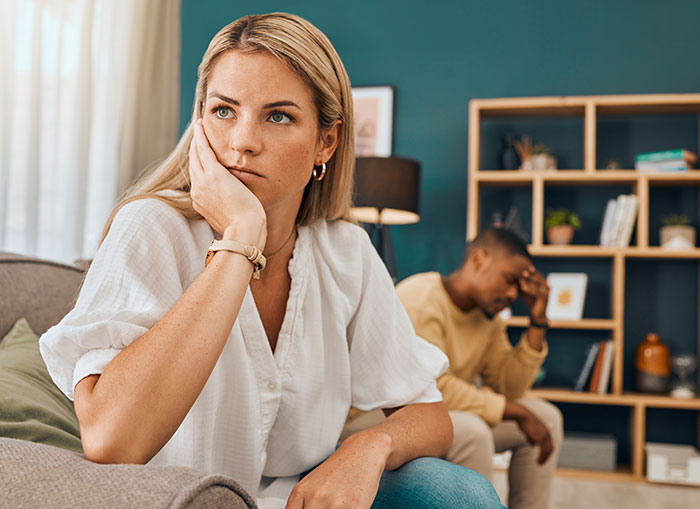 Upset woman looking away while man sits stressed in background, highlighting relationship tension and emotional conflict. Upset woman looking away while man sits stressed in background, highlighting relationship tension and emotional conflict.