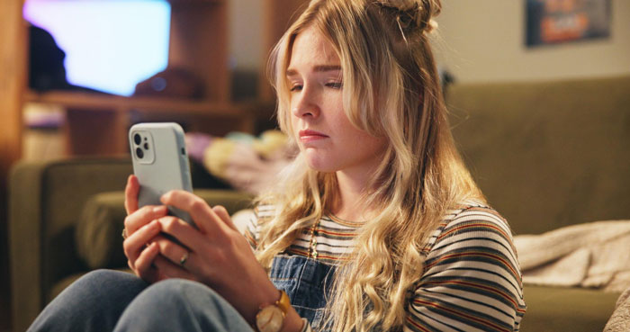 Young woman looking upset while holding a smartphone, illustrating a lady’s unpunctual friend issue.