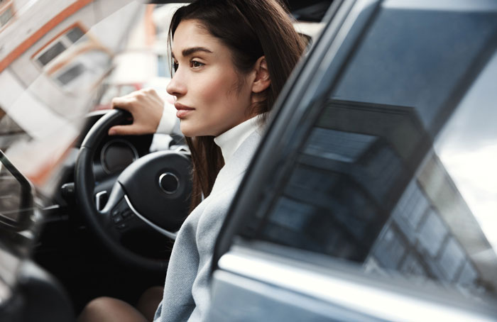 Young woman driving a car, looking thoughtfully outside, reflecting on her unpunctual friend painting nails before event. Young woman driving a car, looking thoughtfully outside, reflecting on her unpunctual friend painting nails before event.