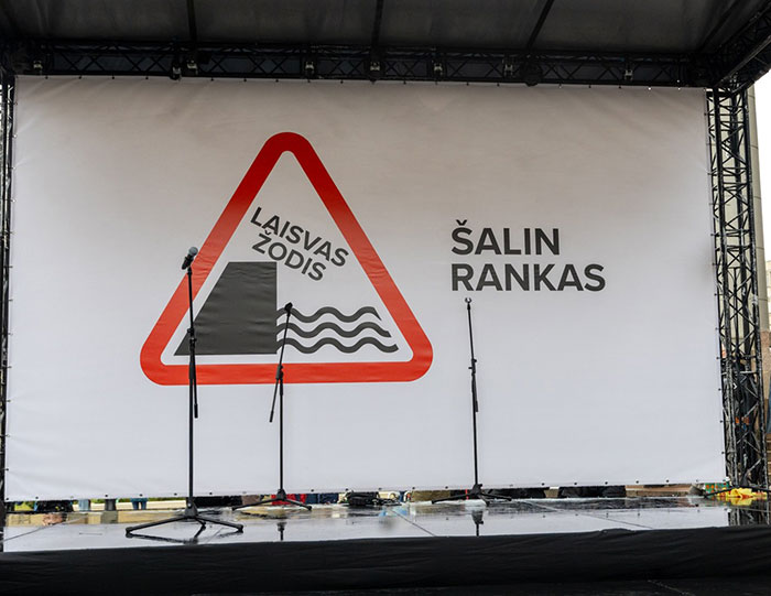 Outdoor stage with microphones and a banner featuring a protest sign related to Lithuania lawmaker’s cat consent. Outdoor stage with microphones and a banner featuring a protest sign related to Lithuania lawmaker’s cat consent.