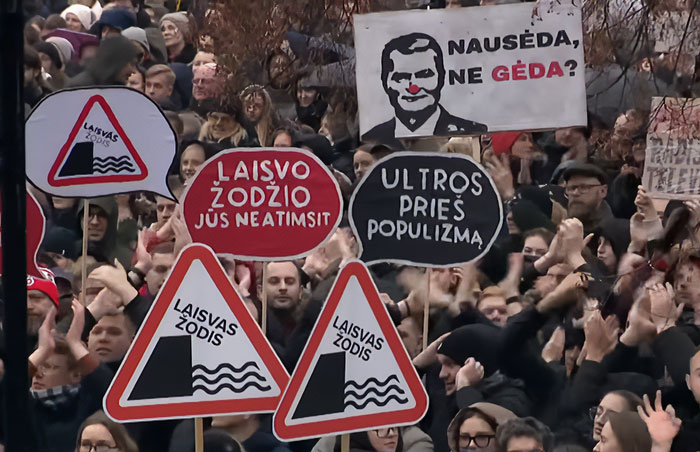 Crowd holding signs in Lithuanian protesting freedom of speech amid lawmaker’s cat consent law for broadcaster dismissal. Crowd holding signs in Lithuanian protesting freedom of speech amid lawmaker’s cat consent law for broadcaster dismissal.
