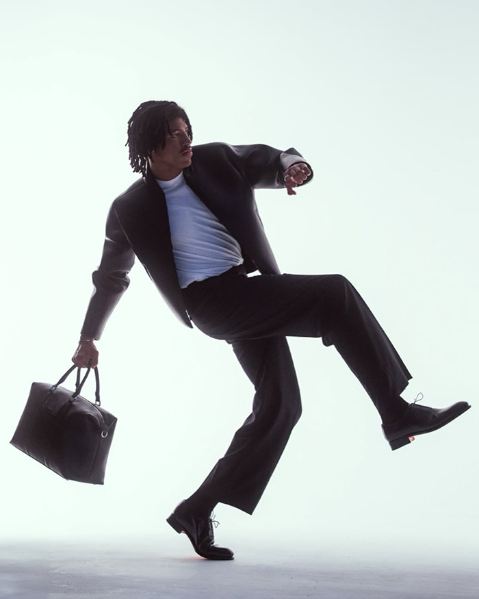 Young man dressed in black and white striking a dynamic pose with a large black bag, modeling fashion style. Young man dressed in black and white striking a dynamic pose with a large black bag, modeling fashion style.