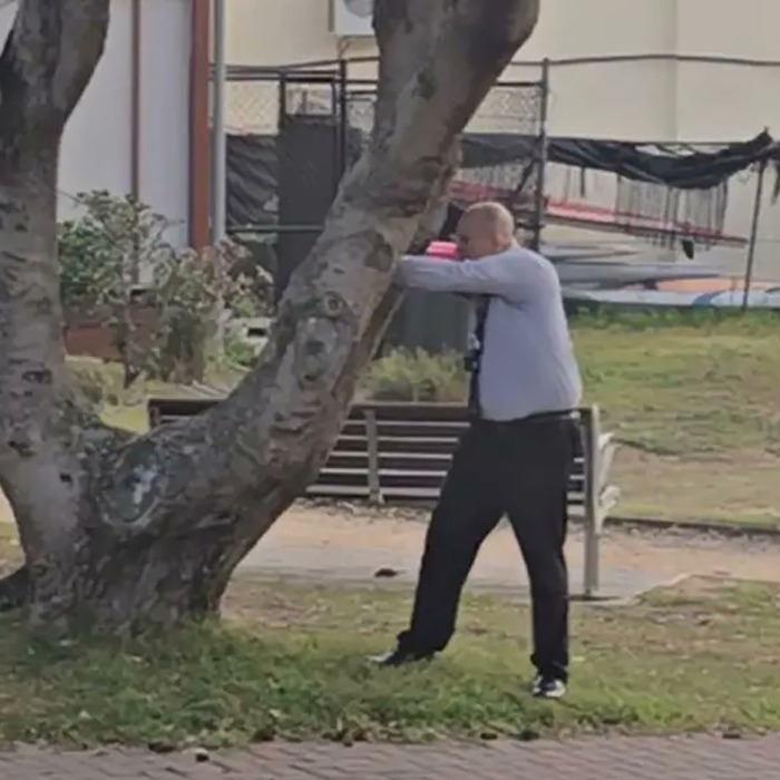 Man in a white shirt and black pants performing a defensive move near a tree, Bondi Beach attacker incident. Man in a white shirt and black pants performing a defensive move near a tree, Bondi Beach attacker incident.