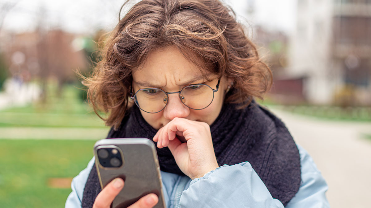 Person with glasses outdoors looking confused at phone, illustrating funny wrong number texts reactions.