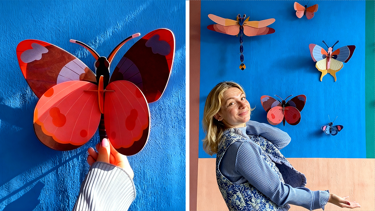 Hand holding a colorful butterfly wall decor with a woman posing by butterfly and dragonfly decorations on blue wall at Hobby Lobby aisle.