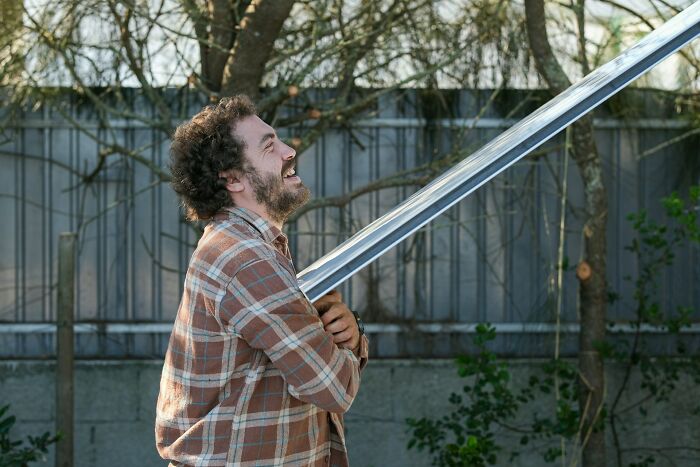 Man with curly hair and beard lifting metal beam outdoors, representing incredible minds without a degree as proof of genius.