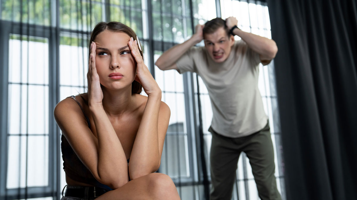 Frustrated woman holding her head while angry husband with trust issues yells behind her in a modern room.