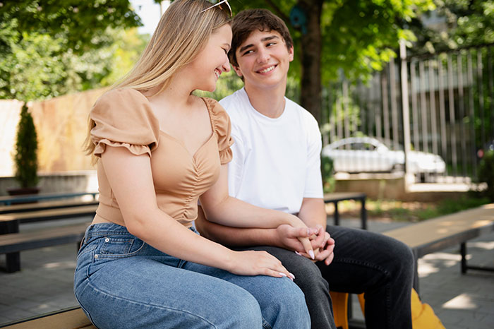 Teen boy and girl smiling and holding hands on a park bench, illustrating dating advice from a dad’s perspective. Teen boy and girl smiling and holding hands on a park bench, illustrating dating advice from a dad’s perspective.