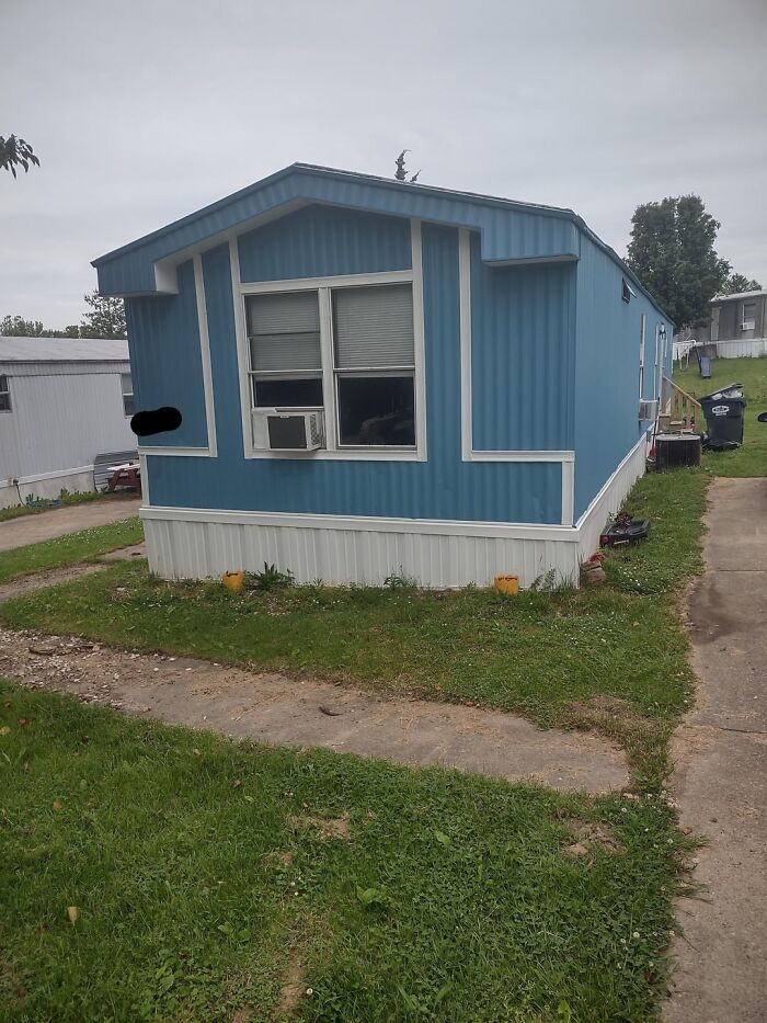 Blue mobile home with white trim in a grassy yard, representing snobbish living contrasted with modest surroundings.