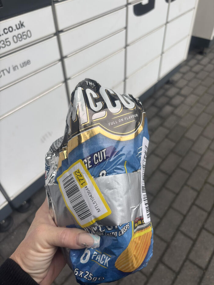 Crumpled McCoy crisps bag with a Vinted shipping label held outside parcel lockers on a paved walkway.