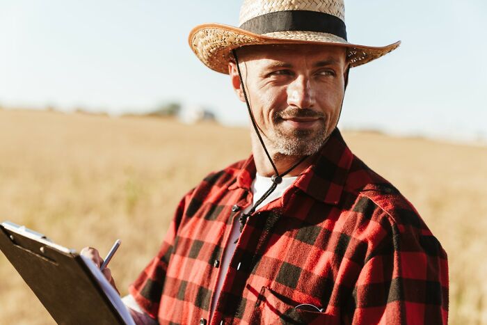Man wearing a straw hat and red plaid shirt, holding a clipboard, representing incredible minds without a degree genius.