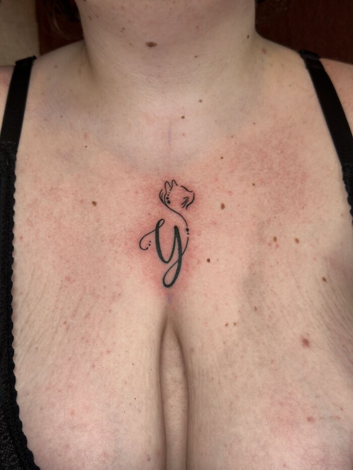 Minimalist pet tribute tattoo of a cat integrated with a letter Y on a person's upper chest, honoring cherished memories.