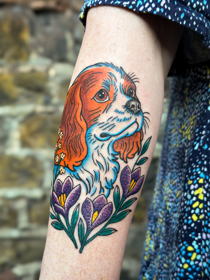 Colorful tattoo of a dog's portrait surrounded by flowers, a beautiful pet tribute capturing memories on a forearm.