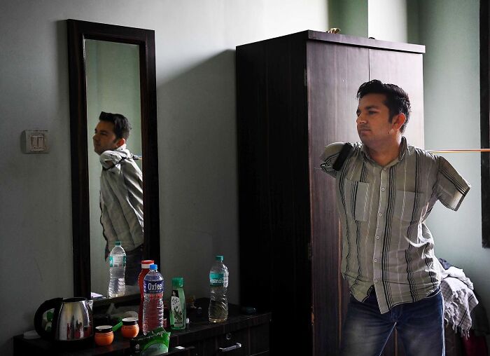 Man with prosthetic arms preparing indoors, showcasing everyday life in Mumbai through a stunning street photo.